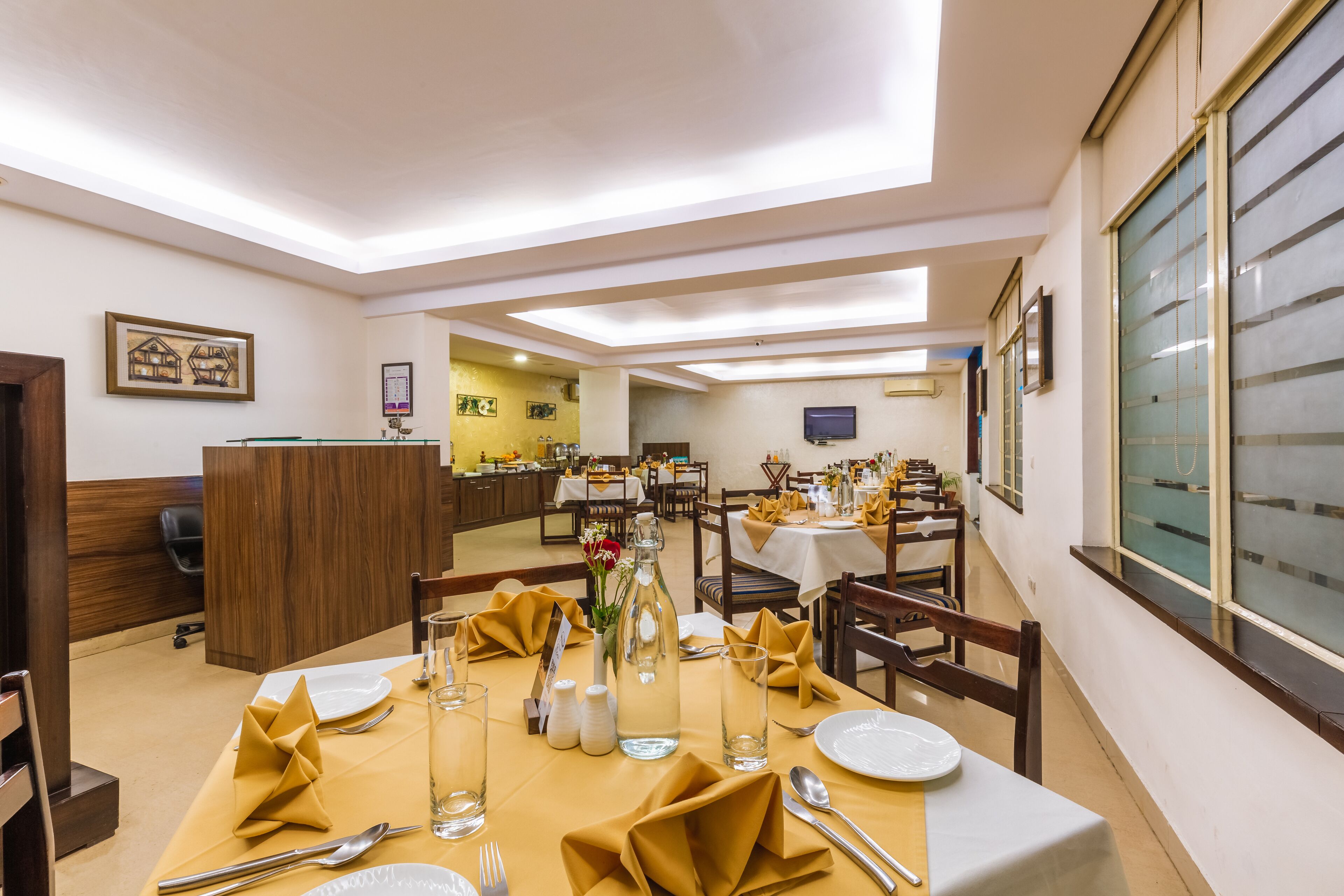 A dining area with tables set for service, a reception desk, and a television on the wall.
