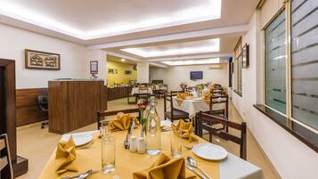 A dining area with tables set for service, a reception desk, and a television on the wall.
