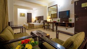 Habitación de hotel con cama, escritorio, televisión y zona de estar con mesa y sillas.