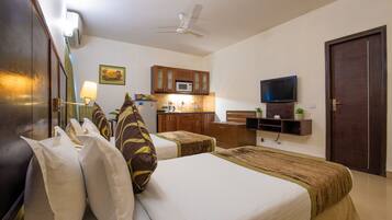 Una habitación de hotel con cama, mesitas de noche, televisión, microondas y un pequeño rincón de cocina.