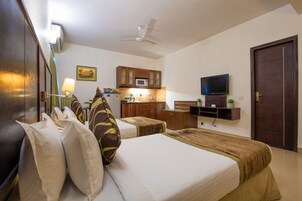 Una habitación de hotel con cama, mesitas de noche, televisión, microondas y un pequeño rincón de cocina.