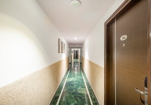 A hotel hallway with a marble floor, a door labeled "141", and framed pictures on the walls. - Rosewood Apartment Hotel - Pantnagar (Kichha)