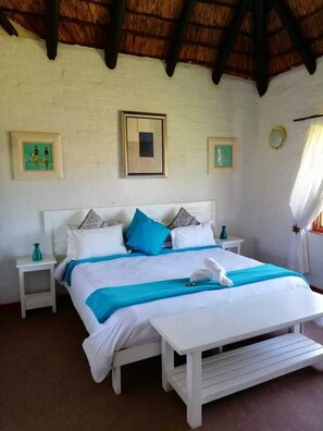 A bed with a white frame, blue bedding, and a towel on the bed. There are two bedside tables with vases on them. - Joie de Vevre Conferences (Paarl)