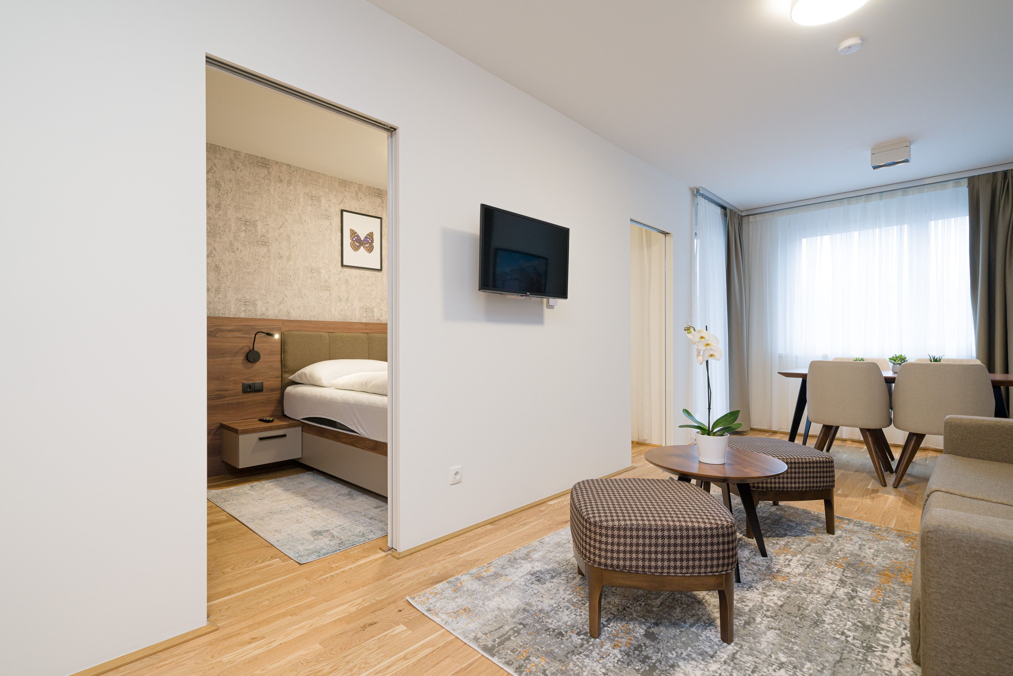 A modern hotel room with a bed, a TV, a dining area with chairs, and a small table.