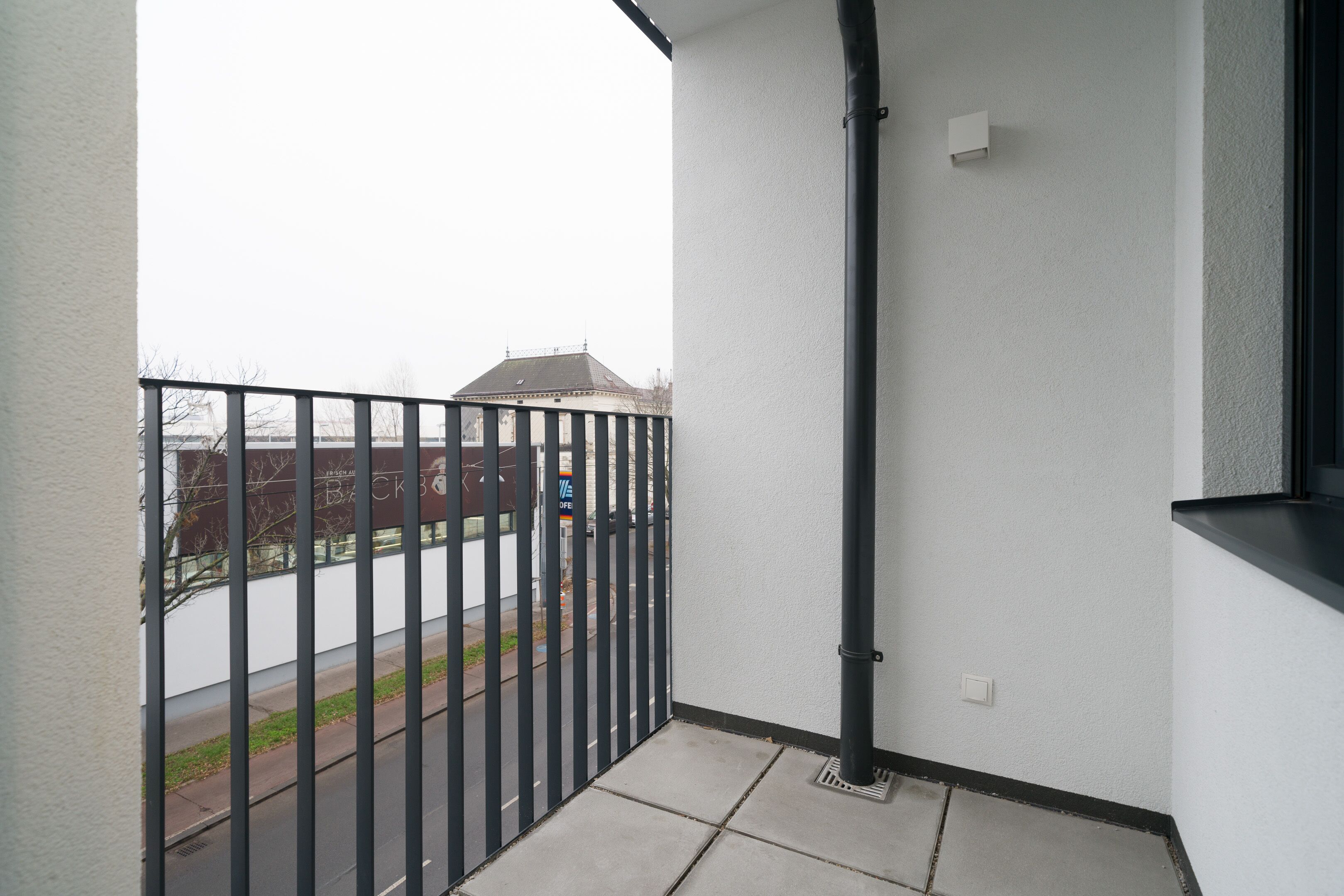 A balcony with a metal railing, a white wall, and a black pipe.