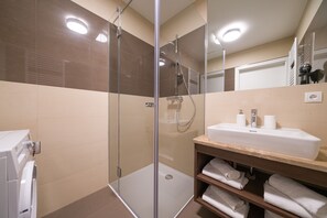 Un baño moderno con ducha de vidrio, un lavabo blanco con encimera de mármol y un perchero con toallas dobladas.