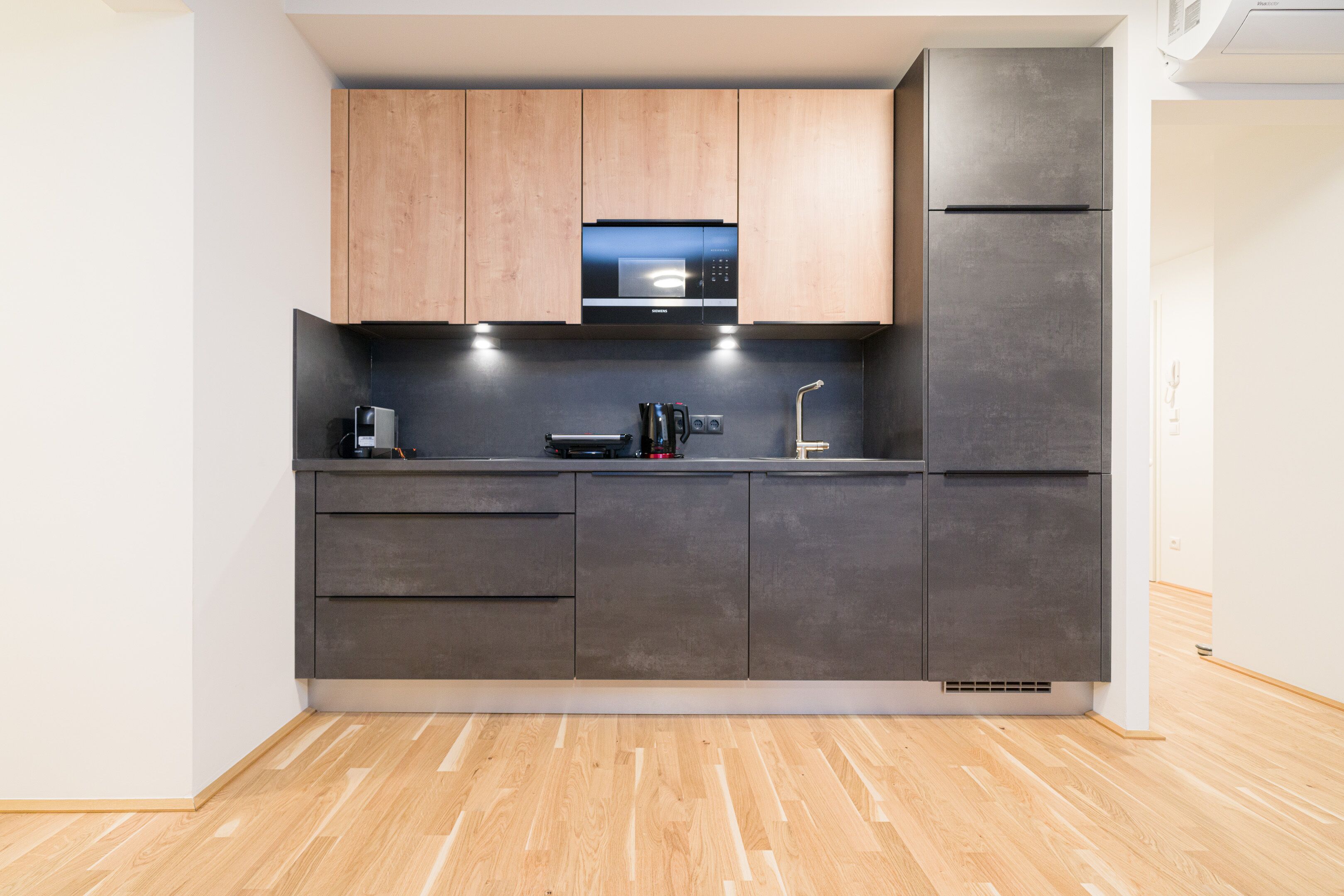 A modern kitchen with wooden cabinets, a built-in microwave, a refrigerator, and a coffee machine.