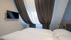 Una habitación de hotel con cama, cortinas, un televisor de pantalla plana y un papel tapiz estampado.
