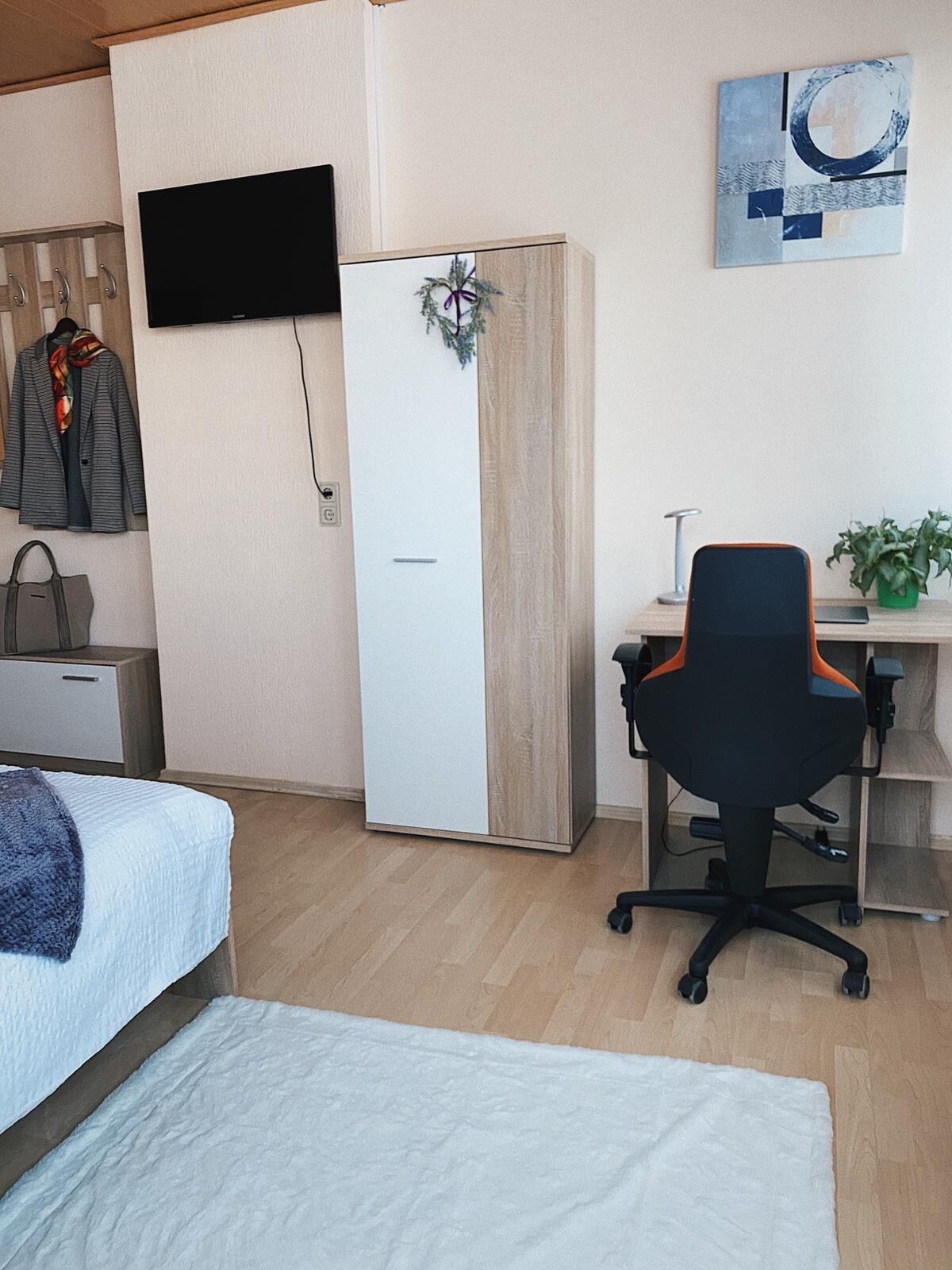 A compact hotel room with a bed, a desk with a chair, a television mounted on the wall, and a wardrobe.