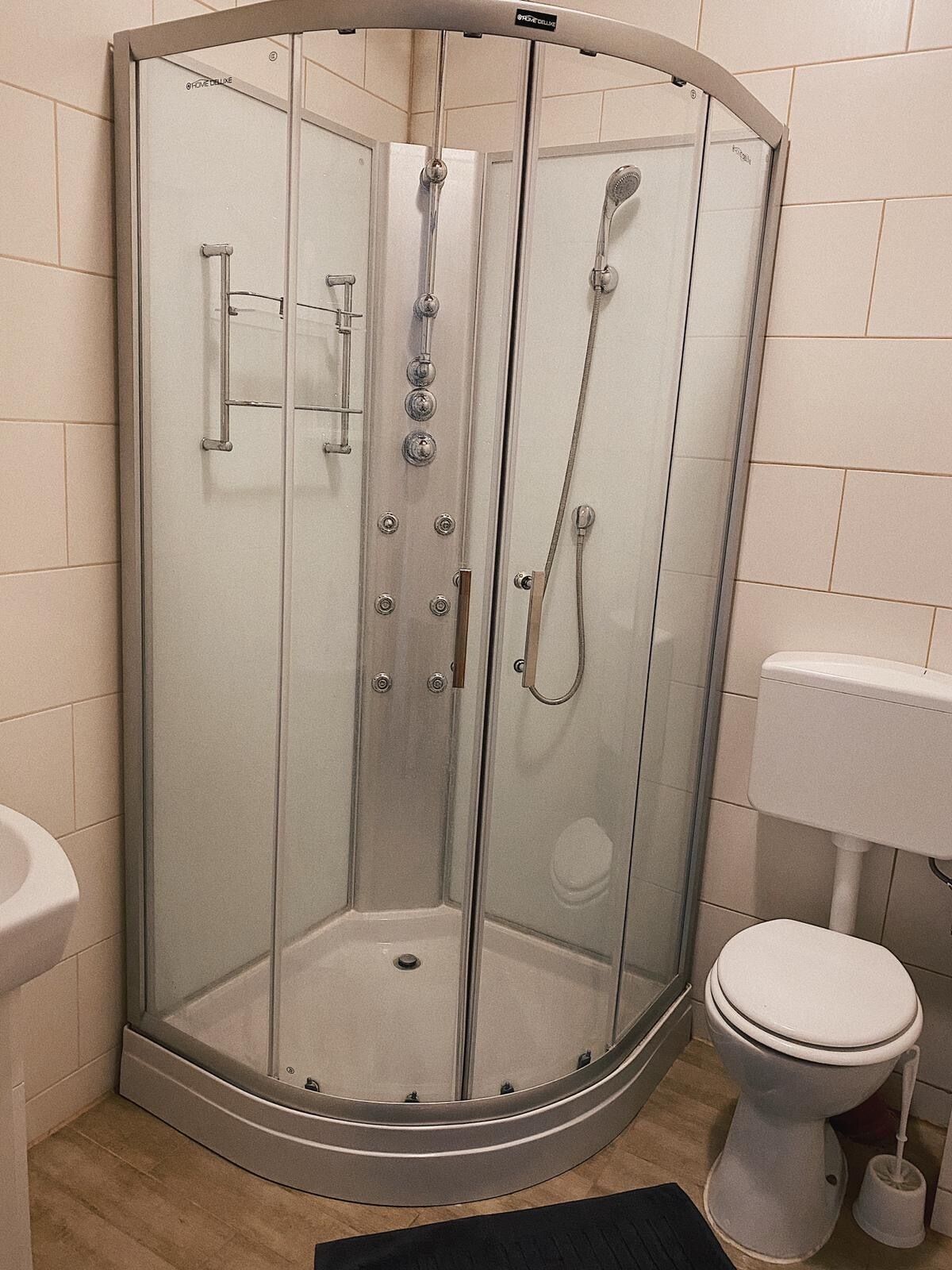 A glass-enclosed shower stall with a toilet and sink in a corner bathroom.