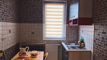 A compact kitchen with a brick wall, a window with blinds, a sink, and a small countertop.