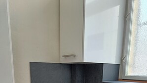 A small kitchen with a black induction cooktop, a kettle, and a white sink. There is a window above the sink and a door on the left. - A Plus Hostel - Centrum (Prague)
