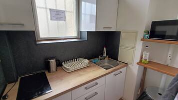 Uma cozinha compacta com janela, chaleira, torradeira, pia e micro-ondas sobre uma bancada de madeira.
