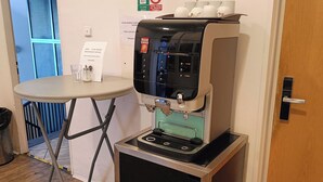 A coffee machine on a cart in a room with a table and a door. - A Plus Hostel - Centrum (Prague)