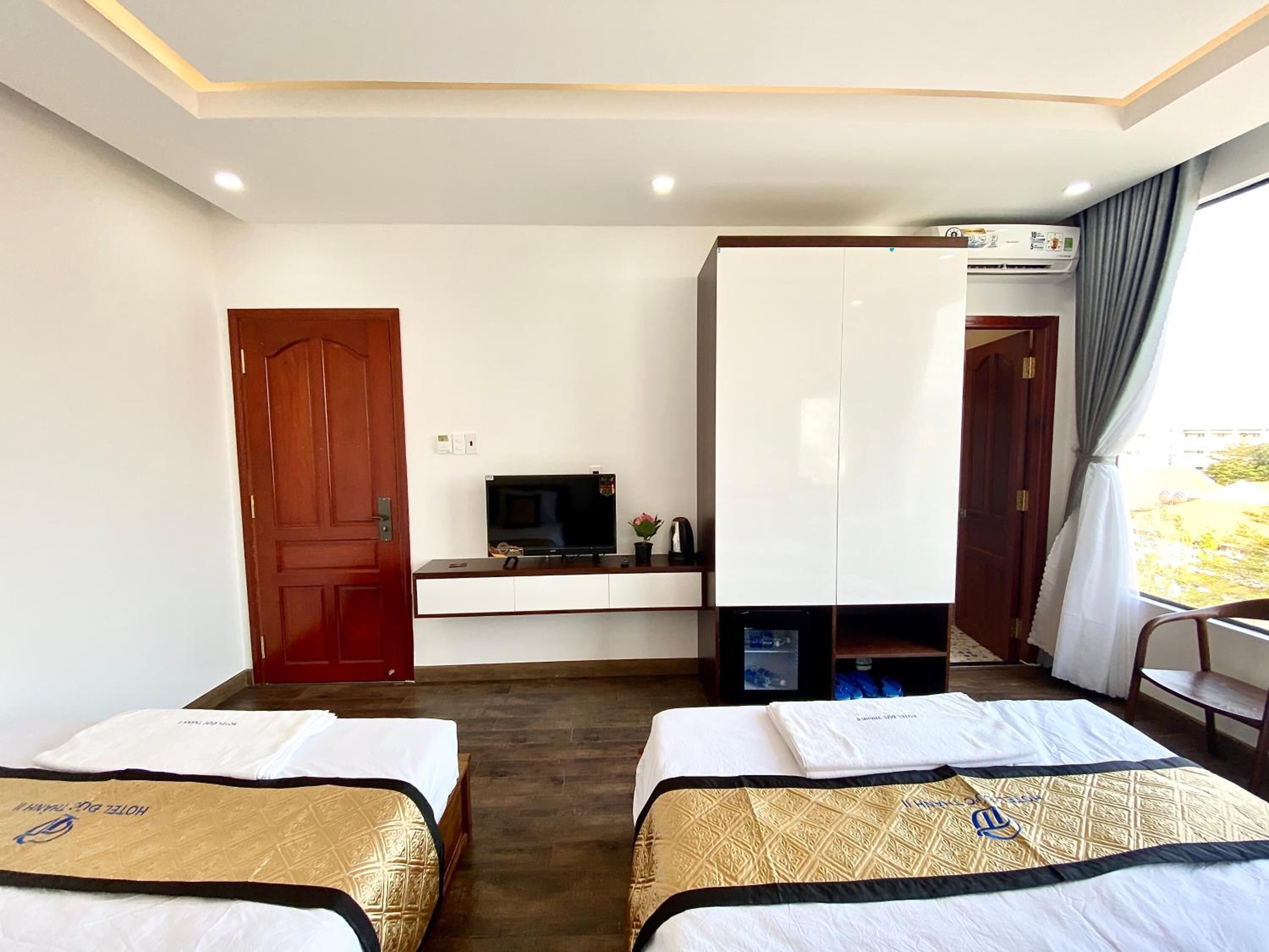 Ein Hotelzimmer mit zwei Betten, einem Fernseher, einem Kleiderschrank, einer Klimaanlage und einem Fenster mit Vorhängen.