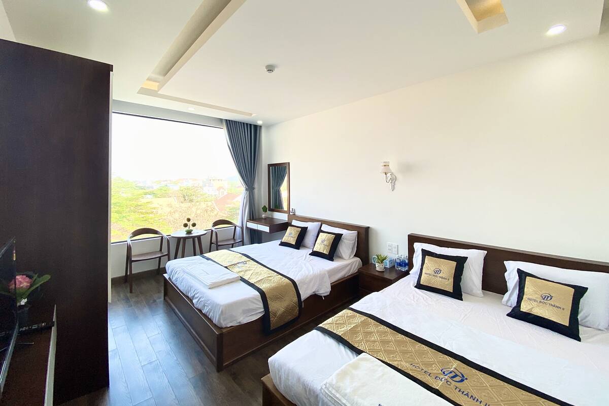 Quarto de hotel com duas camas, uma escrivaninha e uma janela grande.