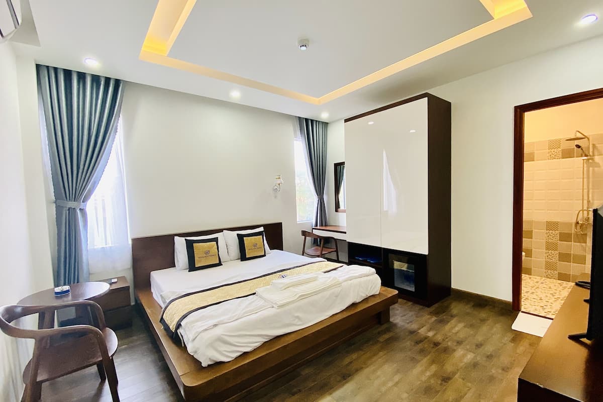 Quarto de hotel moderno com cama de madeira, escrivaninha e área de chuveiro.