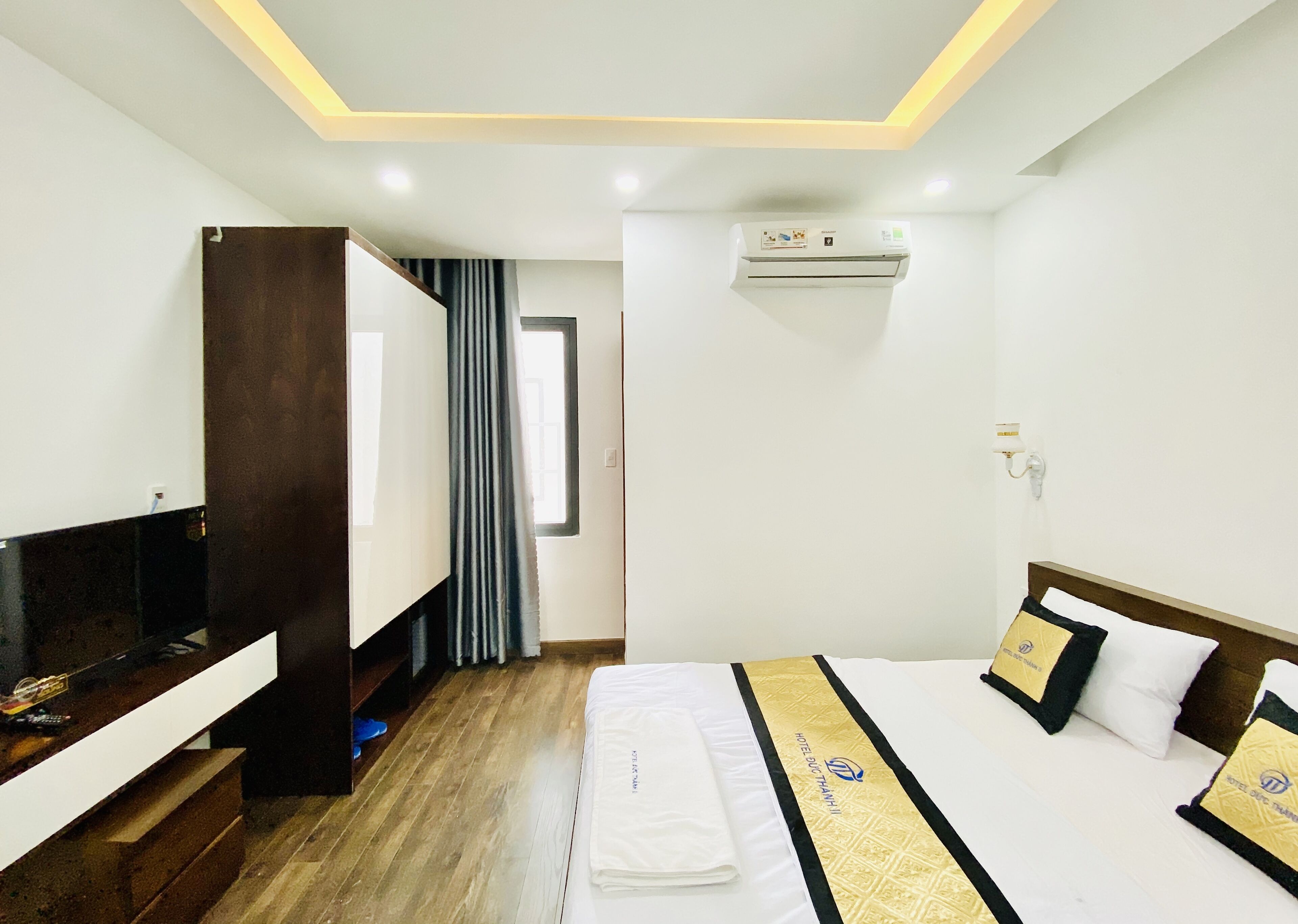 A hotel room with a bed, a desk, a wardrobe, and an air conditioning unit.