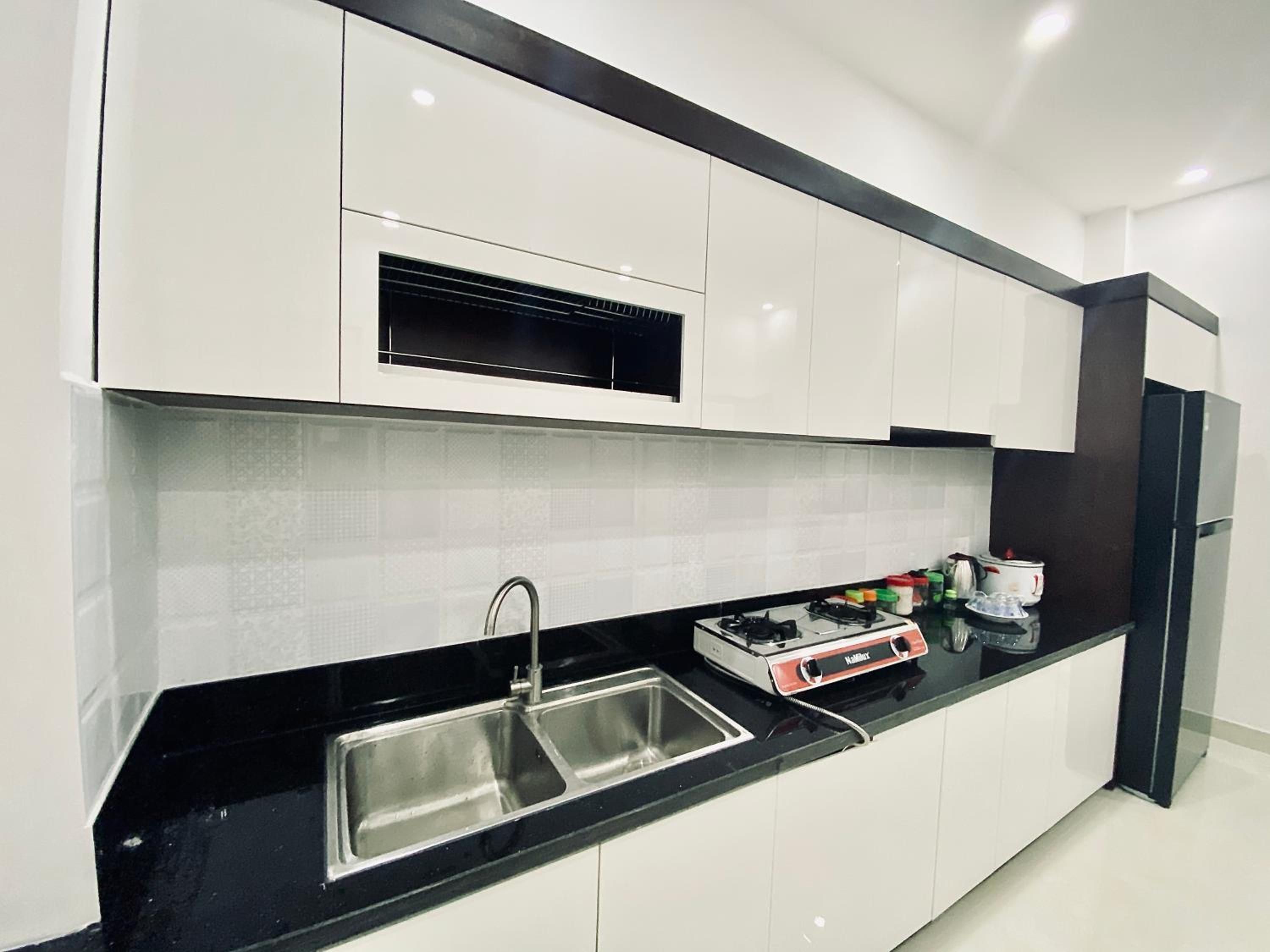 Una cocina moderna con armarios blancos, encimera negra, pileta de acero inoxidable y estufa integrada.