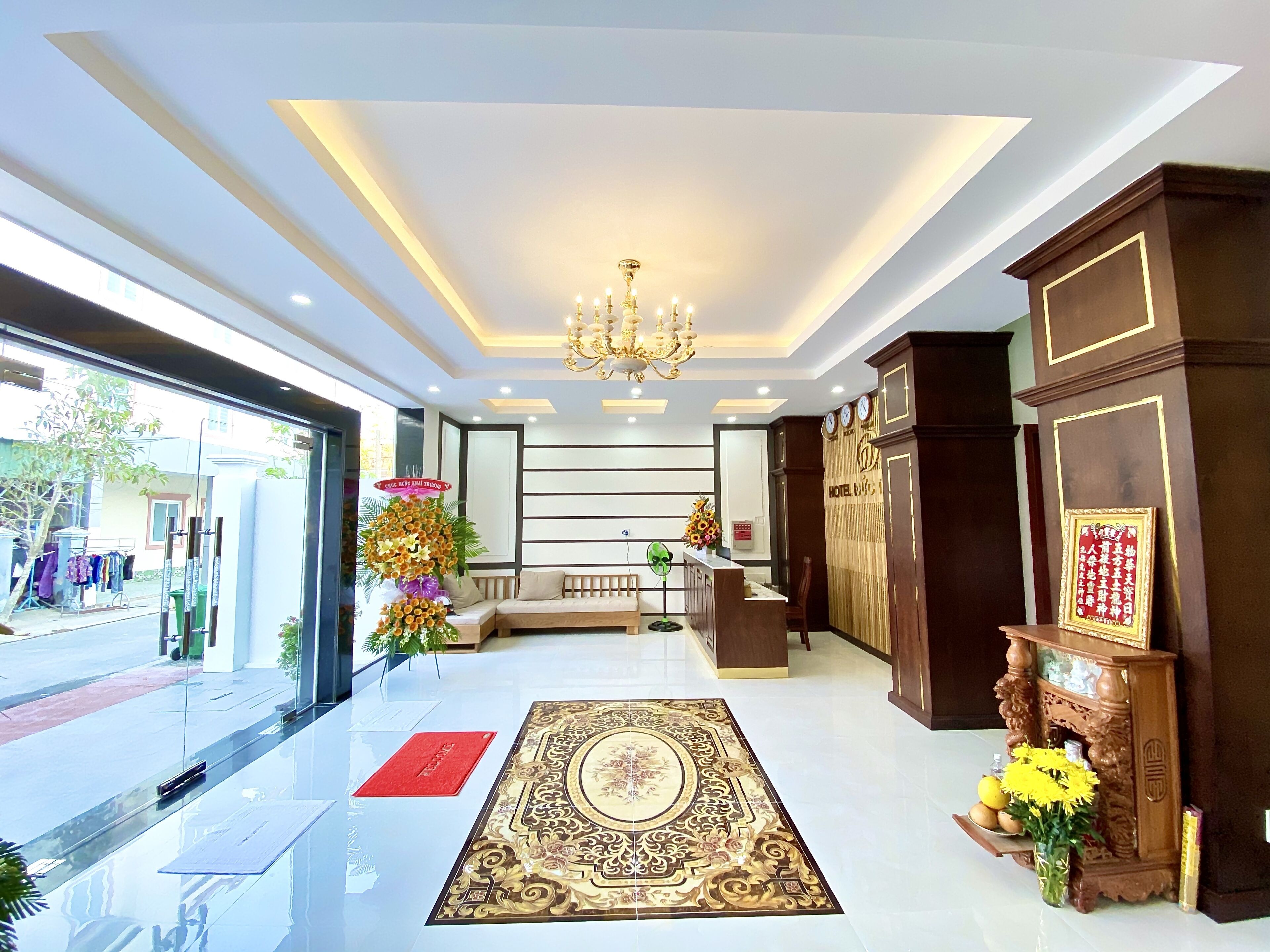 A hotel reception area with a chandelier, a reception desk, a sofa, and a decorative rug.
