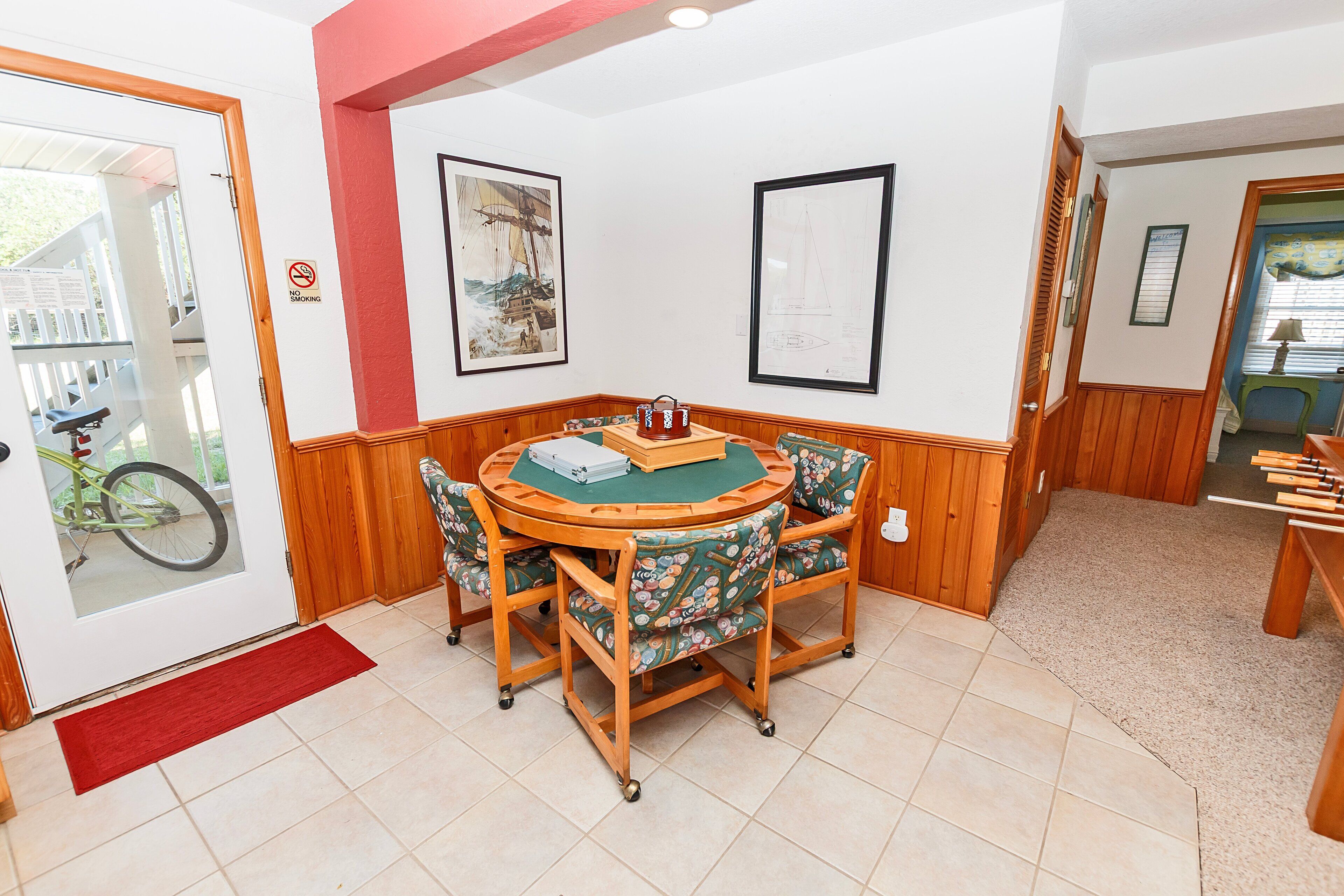 A room with a round wooden table, four chairs, and two framed artworks on the wall.