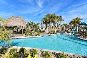 A swimming pool with a slide, surrounded by palm trees and a thatched-roof structure. - Projection Screen Loft • Game Room • Private Pool & Spa • Near Disney (Davenport)