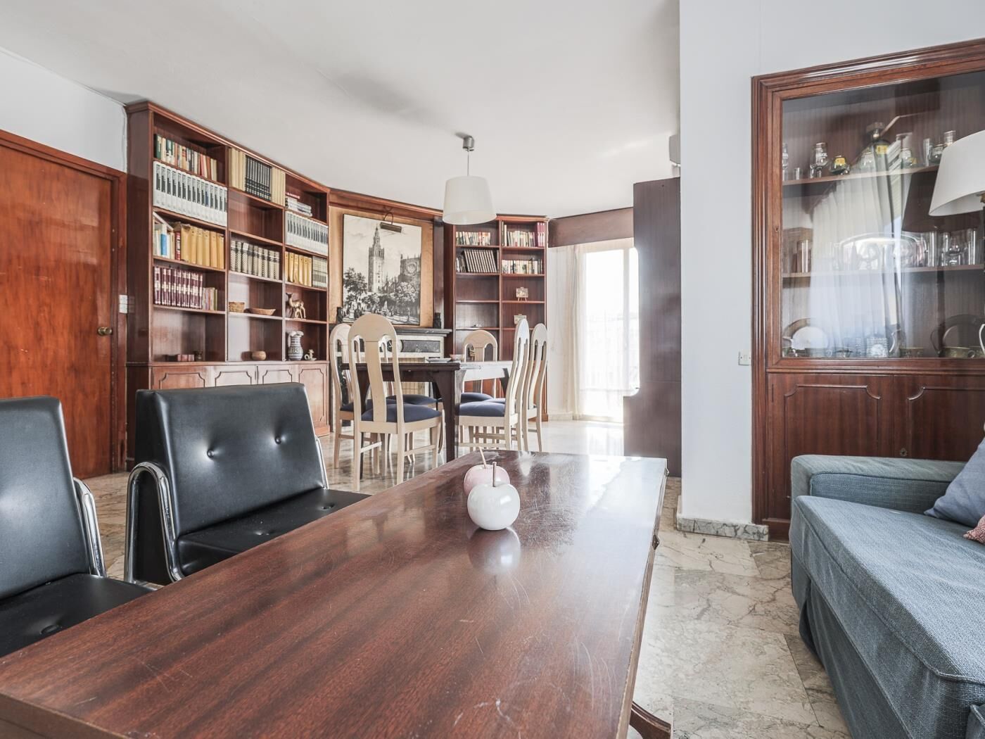 Una habitación con una mesa de comedor de madera, sillas, una estantería y un sofá.