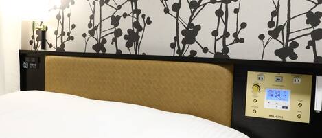Habitación de hotel con cama, panel de control de aire acondicionado y pared con estampado floral oscuro.