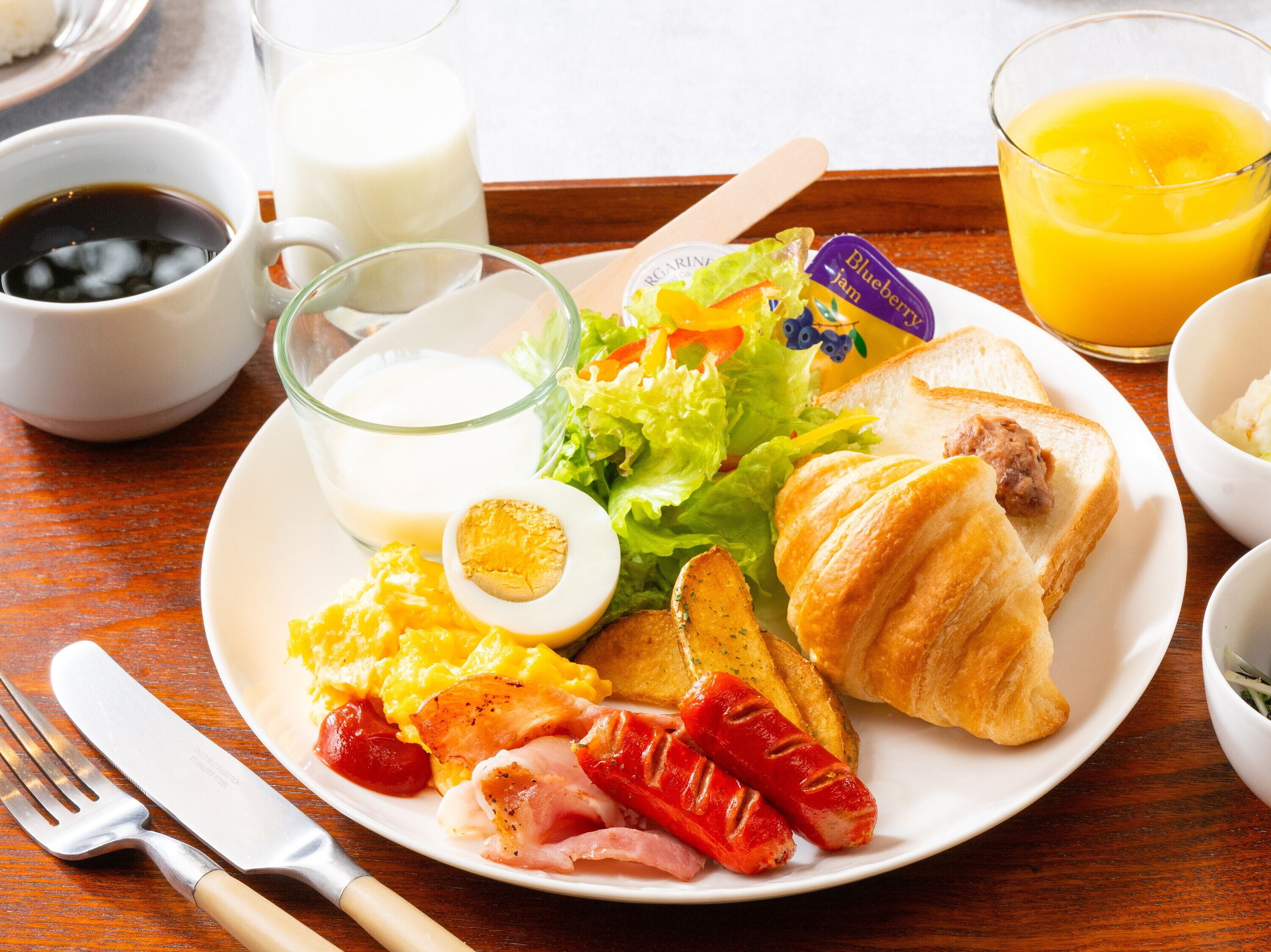 Een ontbijt bord met eieren, spek, worst, toast en een glas sinaasappelsap.