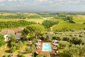 An aerial view of a property with a swimming pool surrounded by lounge chairs and umbrellas, set in a lush green landscape with vineyards and rolling hills in the background. - Villa Bagnano (Certaldo)