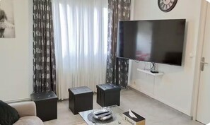 A living room with a flat-screen TV, two black ottomans, a coffee table with a decorative bowl, and a tissue box. - Your perfect cocoon 9 min from Eurexpo and 14 min from Groupama (Saint-Priest)