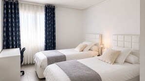 Hotellihuone, jossa on kaksi sänkyä, työpöytä ja tuoli.