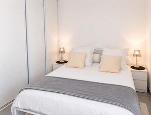 Un dormitorio ordenado con una cama, dos mesitas de noche y dos lámparas.