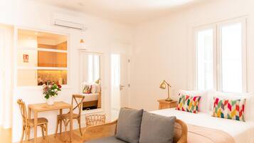 Una habitación luminosa y bien iluminada con una cama, un sofá, una mesa de comedor con sillas y una mesita de noche con una lámpara.