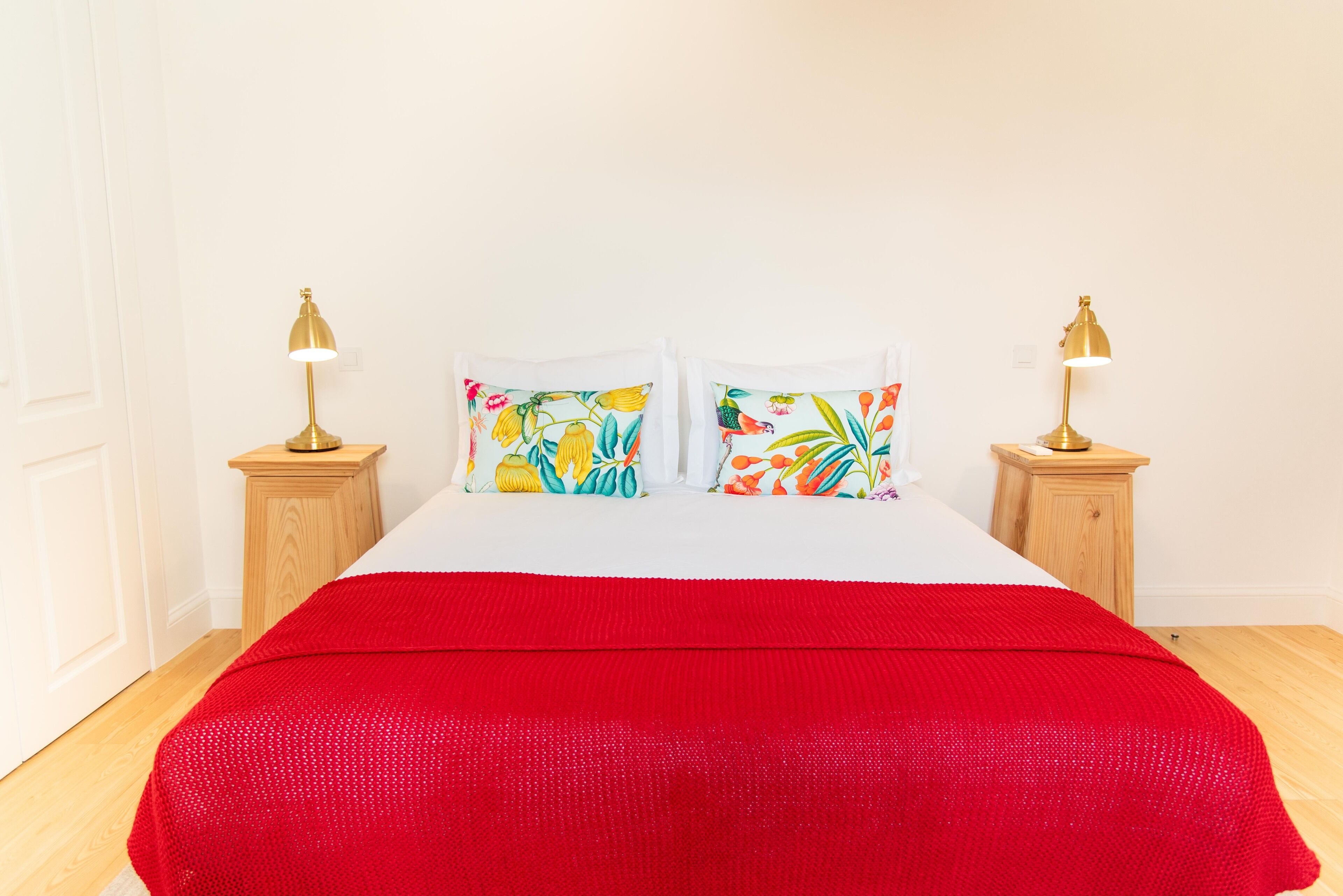 A bed with a red blanket, two nightstands with lamps, and two pillows with floral designs.