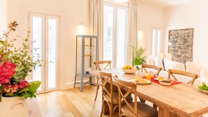 A dining area with a wooden table, chairs, a vase of flowers, and a bowl of fruit. - Apartamentos Ferreiros (Funchal)