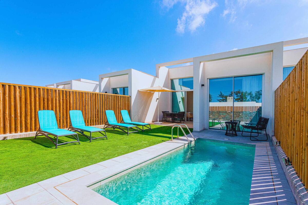 Ein moderner Poolbereich mit einem klaren, blauen Pool, grünem Kunstrasen und blauen Liegestühlen.
