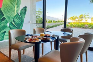 A breakfast setting with a table, chairs, and a view of a garden through large windows. - Resort Cordial Santa Agueda & Perchel Beach Club (San Bartolomé de Tirajana)