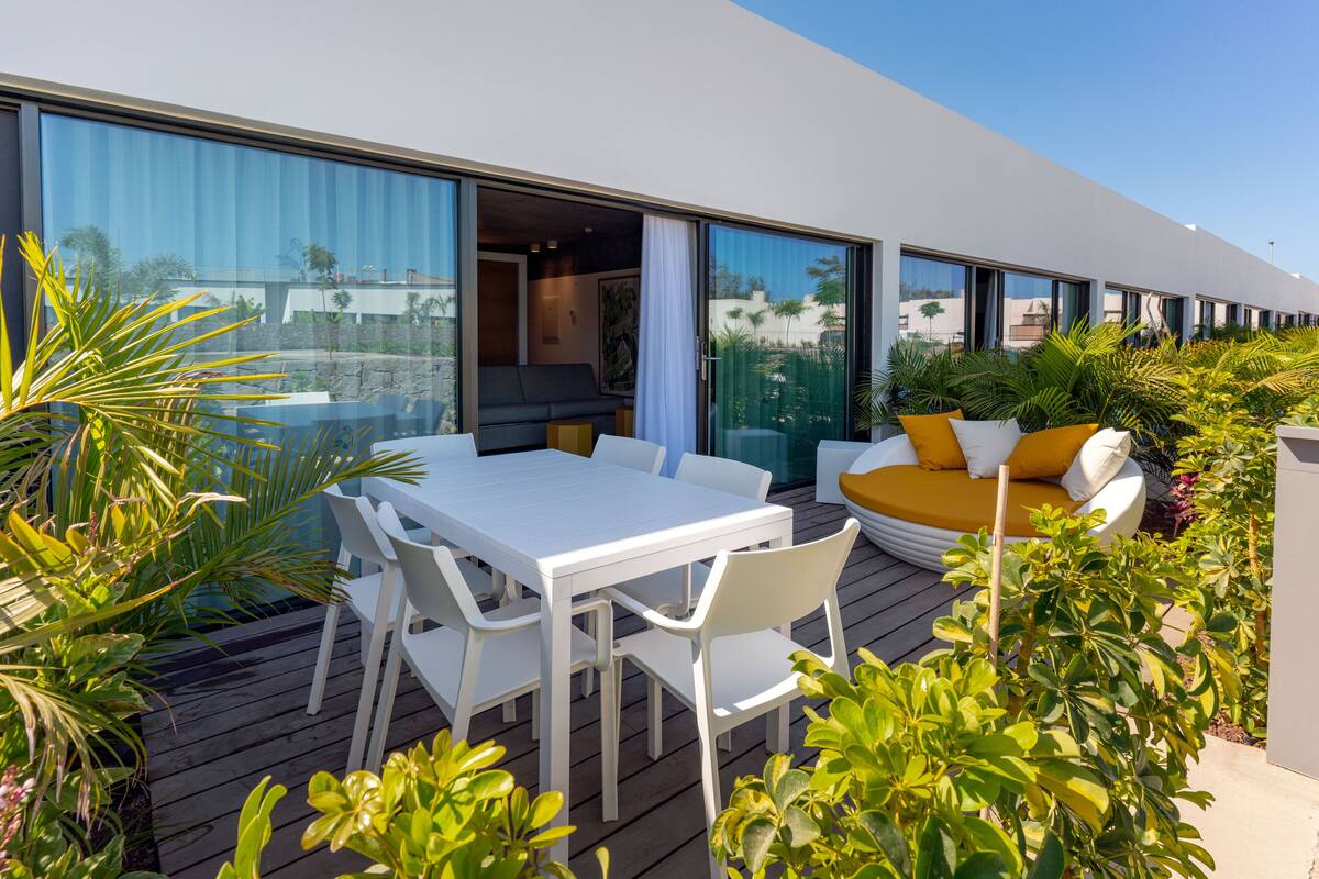Eine moderne Außenpatio mit einem weißen Tisch und Stühlen, einem gelben Sofa und üppigem Grün.