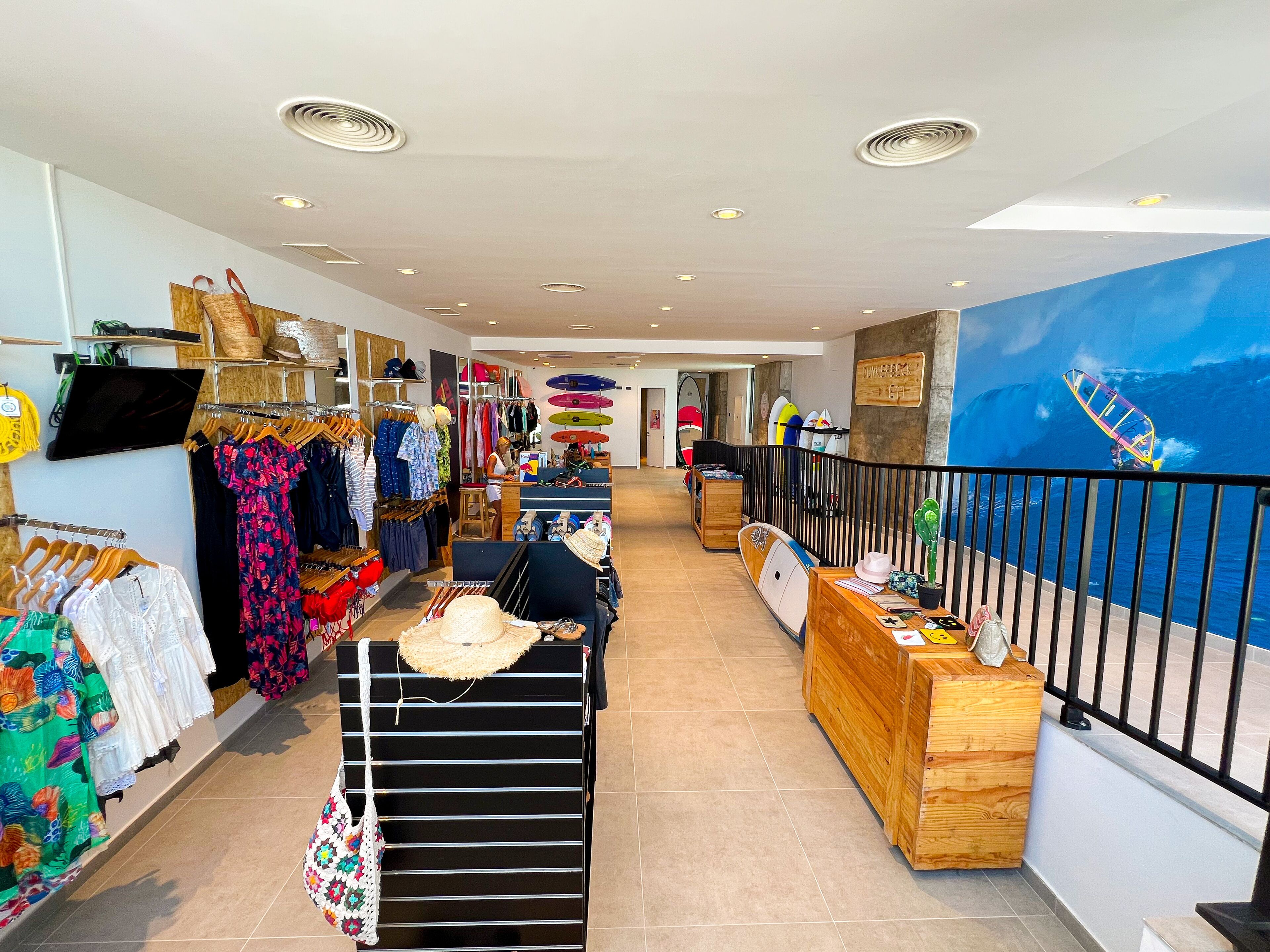Un magasin de vêtements avec des portants remplis de robes, un comptoir en bois et une fresque représentant un surfeur sur une vague.