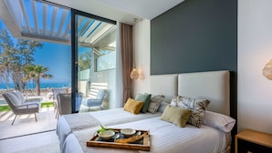 Une chambre moderne avec un grand lit, un plateau contenant des articles pour le petit-déjeuner, une vue sur l’océan et une terrasse avec des sièges d’extérieur.