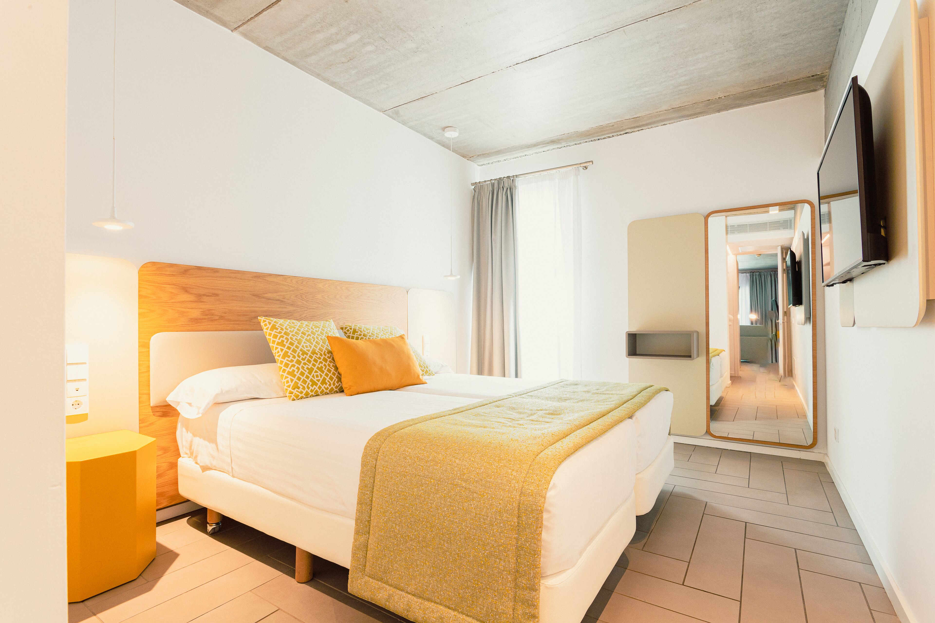 A hotel room with a bed, bedside table, and a mirror.