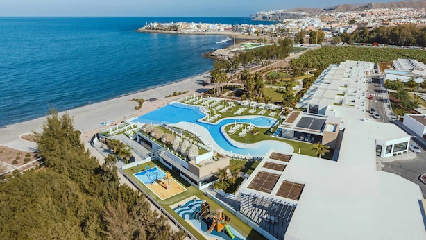 Vue aérienne d’une station balnéaire avec une piscine, une plage et des bâtiments modernes.