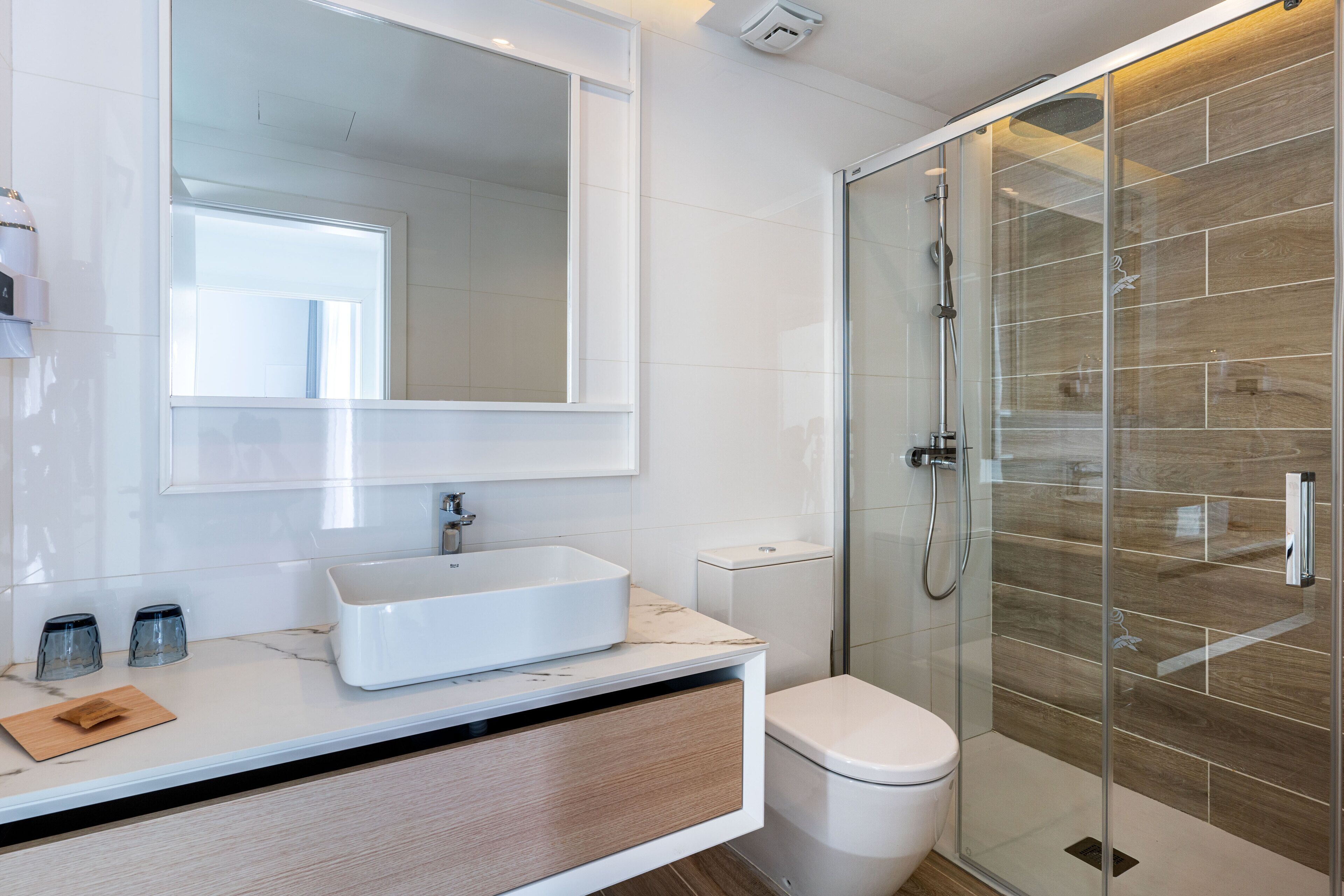A modern bathroom with a large mirror, a white sink, a toilet, and a glass-enclosed shower.