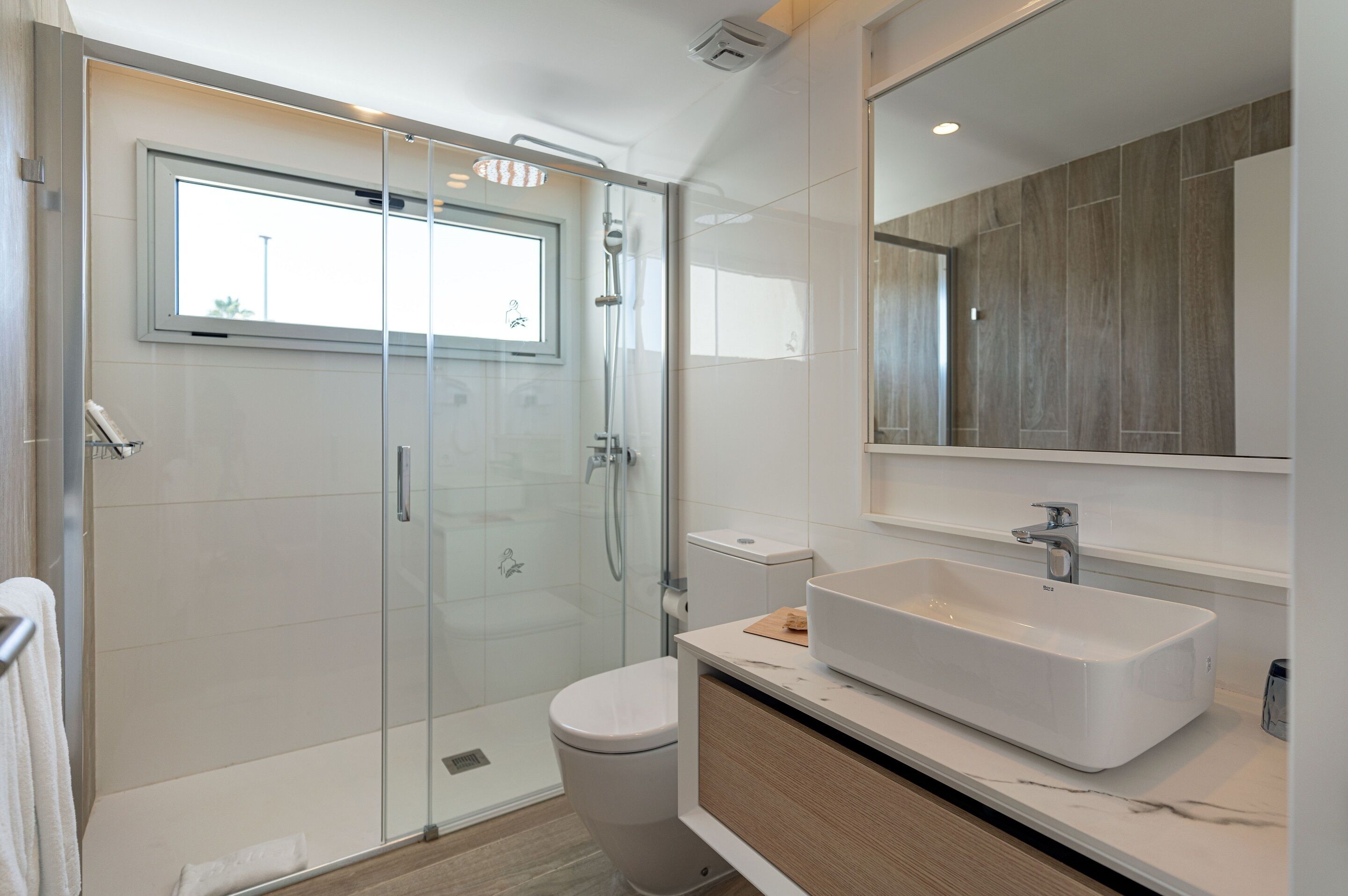 A modern bathroom with a glass-enclosed shower, a white sink, and a large mirror.
