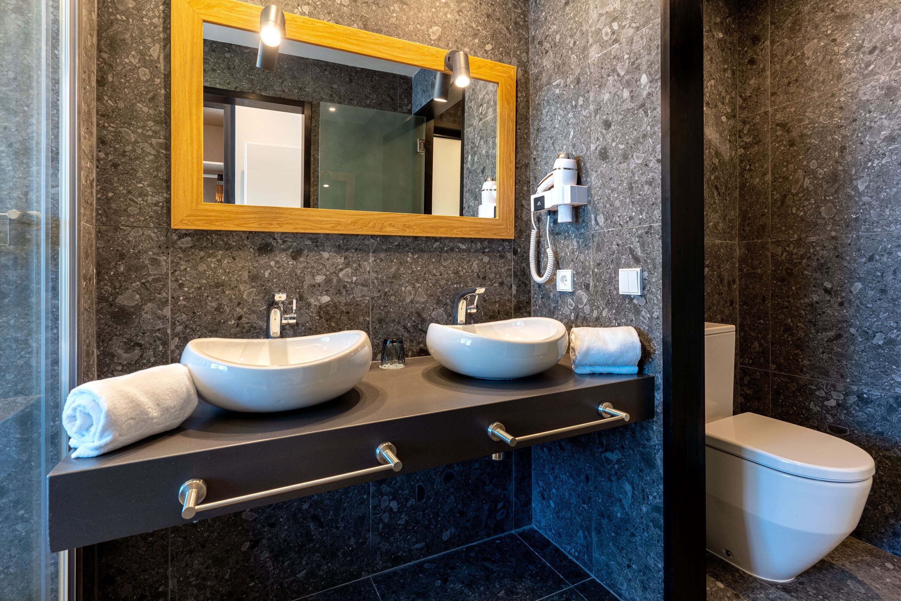 A modern bathroom with two sinks, a mirror, and a toilet.