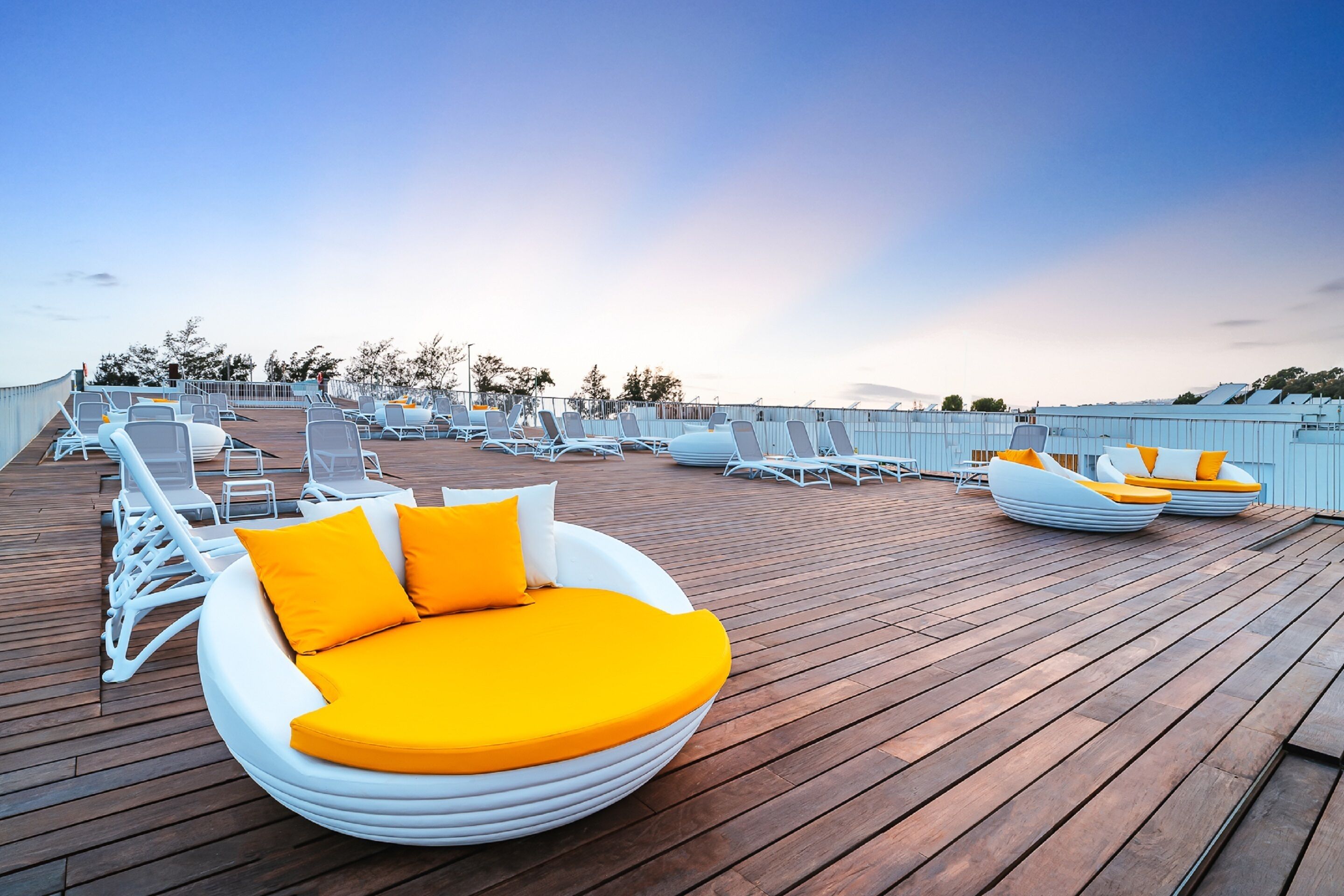 A rooftop lounge area with white lounge chairs and a circular seating area with orange cushions.