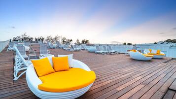 A rooftop lounge area with white lounge chairs and a circular seating area with orange cushions.
