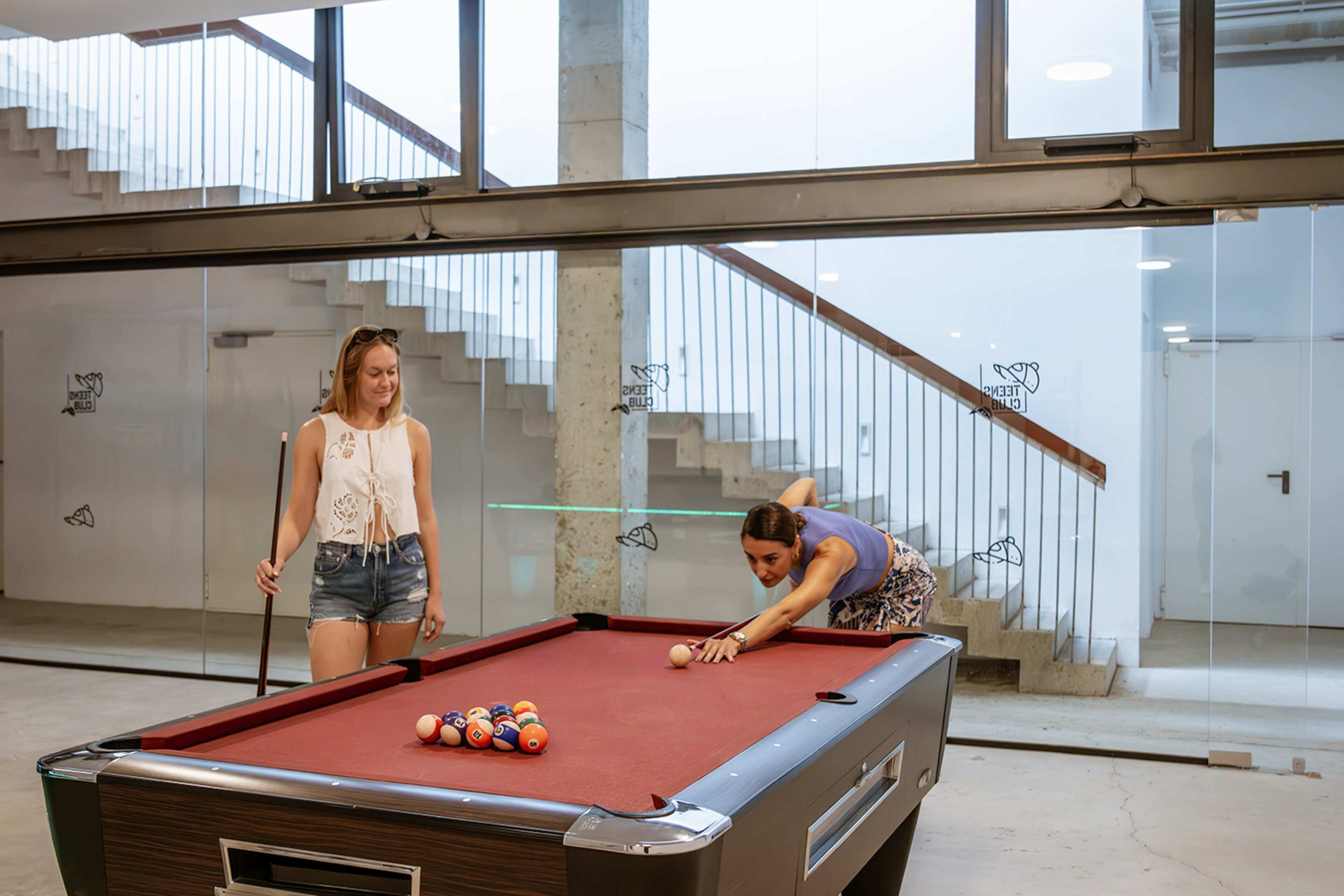 Een pooltafel in een moderne binnenruimte, met een glazen wand en een trap op de achtergrond.