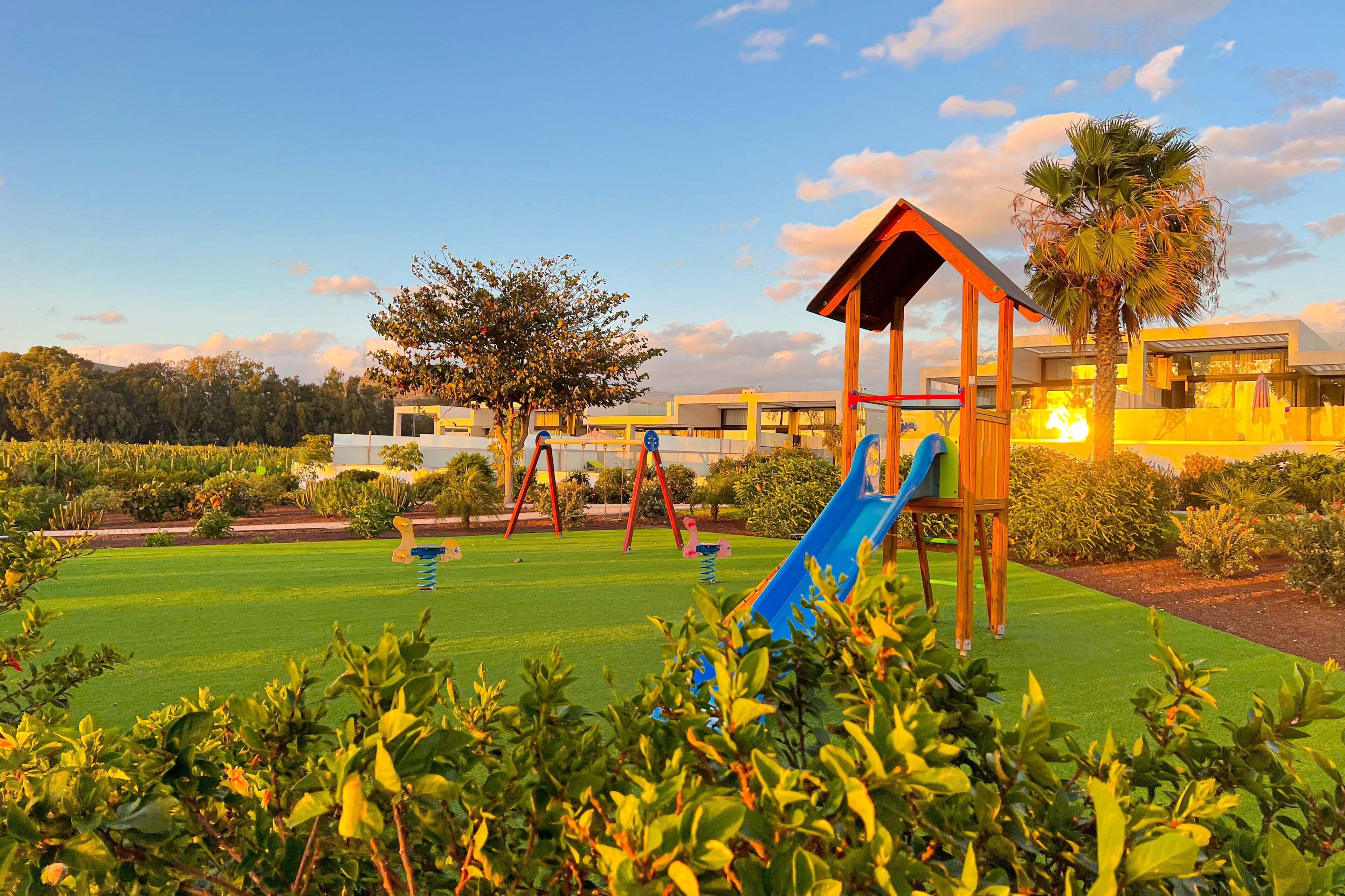 A playground with a slide and swings, surrounded by well-maintained grass and trees.